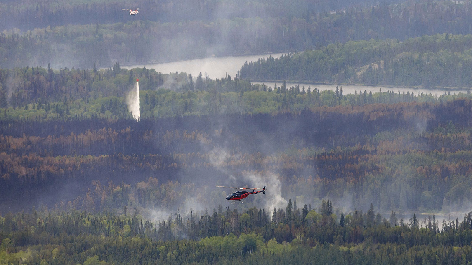 Helicopter and airplane flying above wildfire smoke