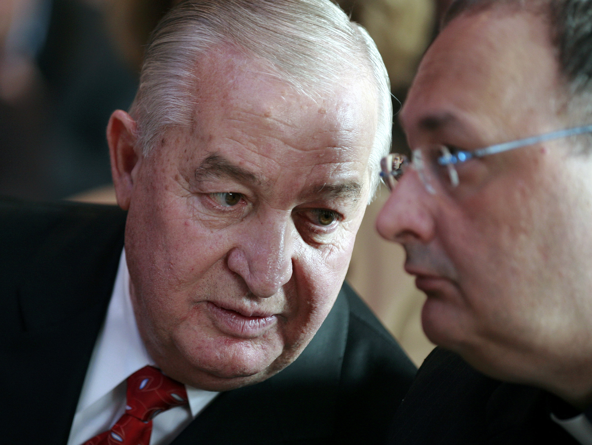Louis DeNaples, wearing a suit and tie, leans over to speak to a man next to him.