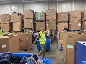 Marisa Adler posing in a textile sorting facility surrounded by cardboard boxes