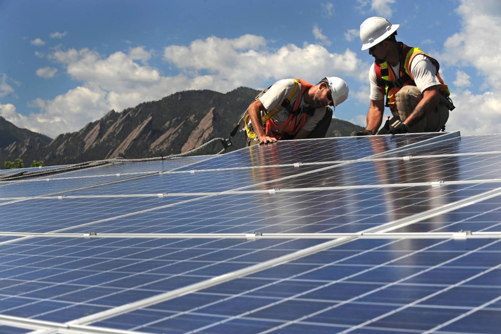 A closeup of two men installing solar panels on a roof with mountains in the background