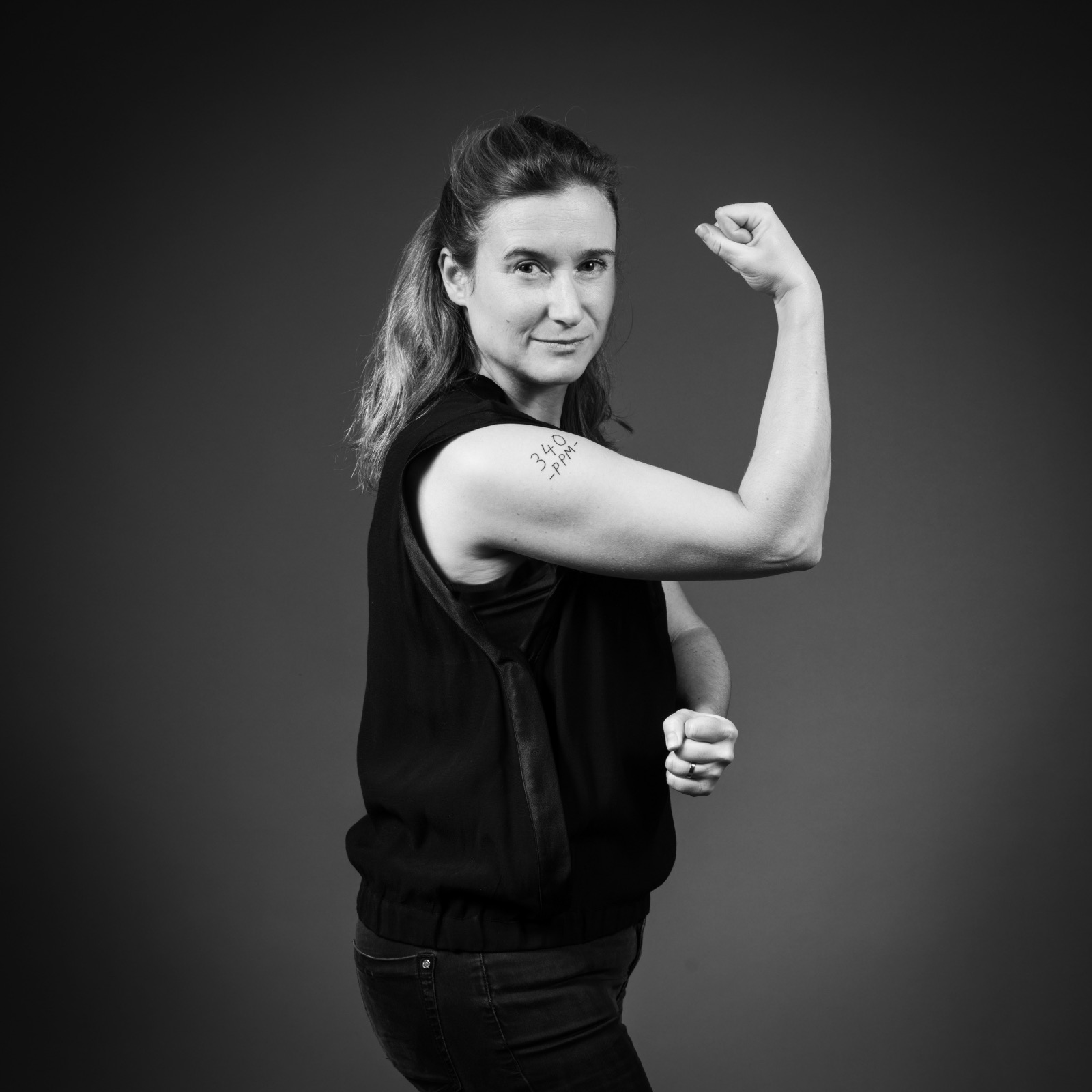 A woman with her arm raised in a fist, showing the 340 PPM tattooed on her bicep