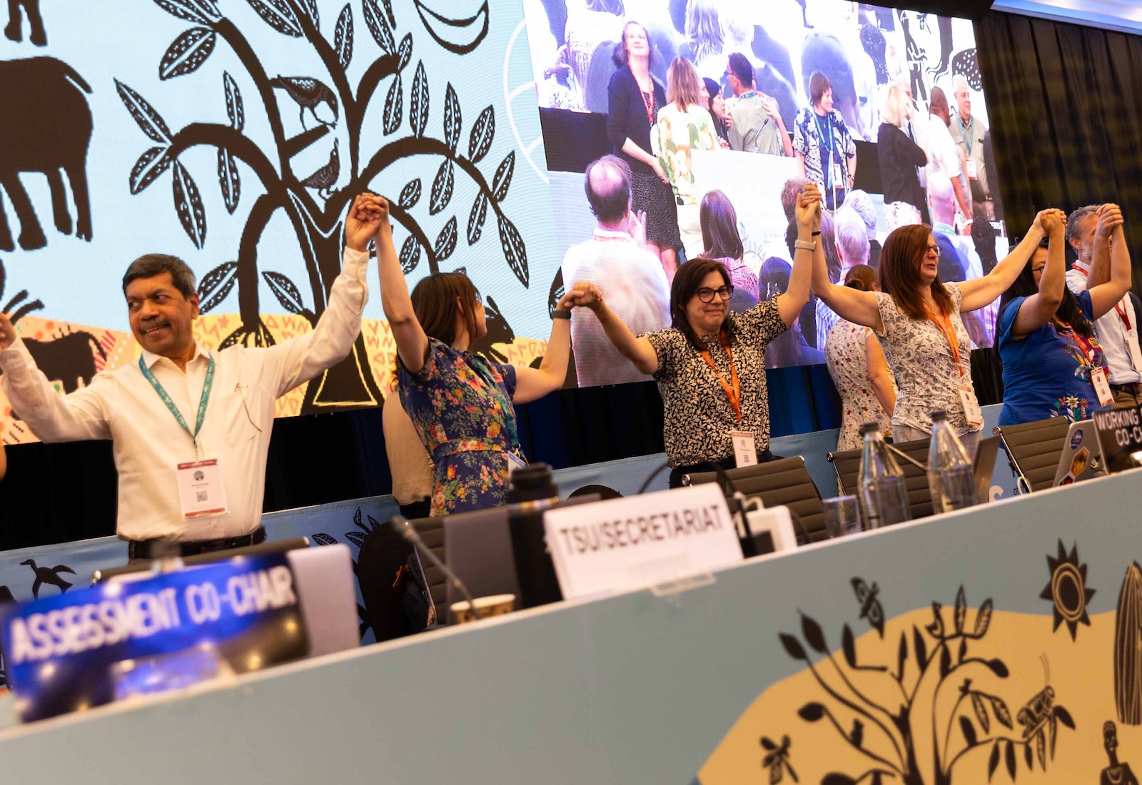 People stand behind a table holding hands in celebration.