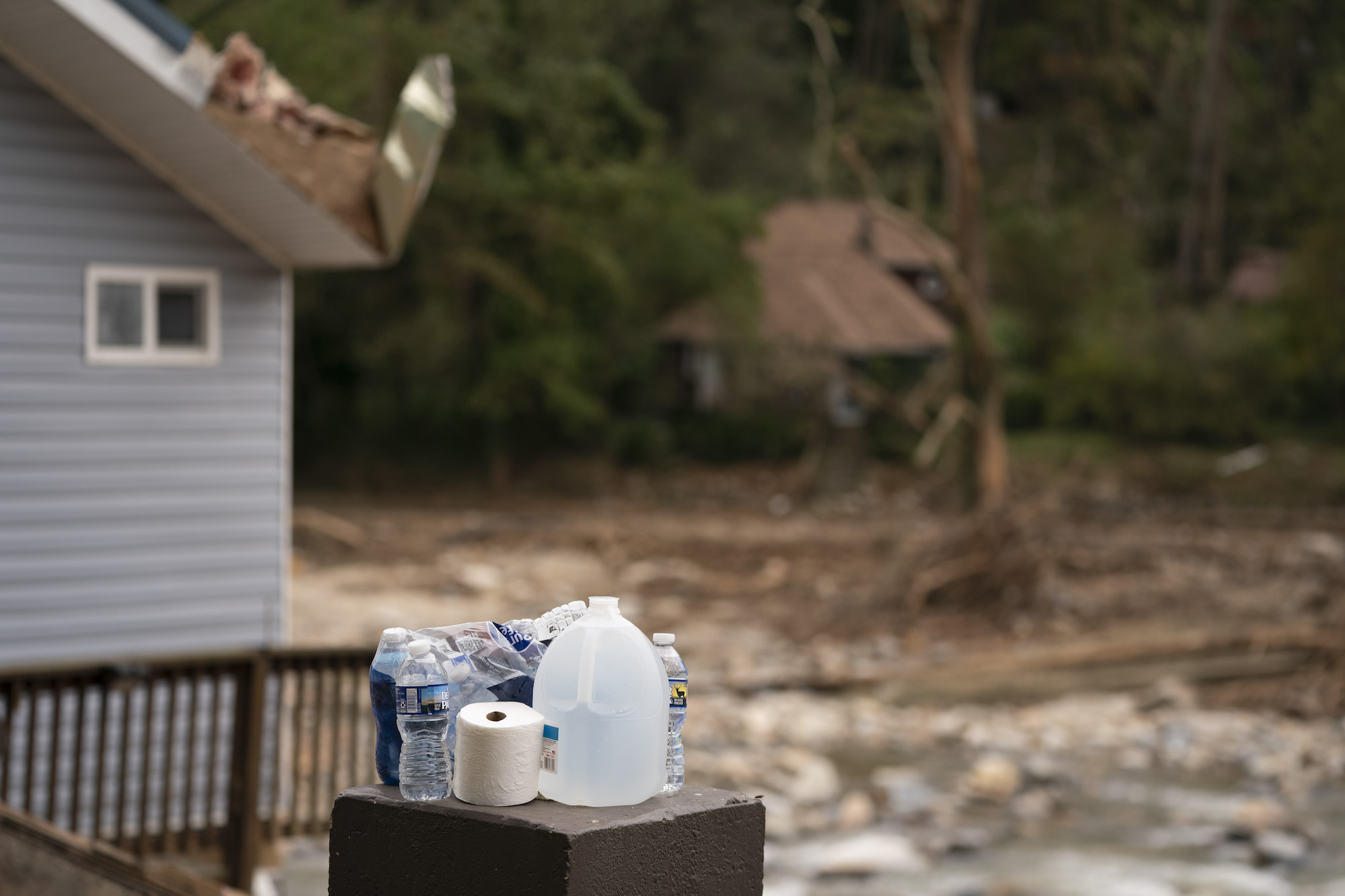 Bottled water and a toilet paper roll sit on a small box near a house