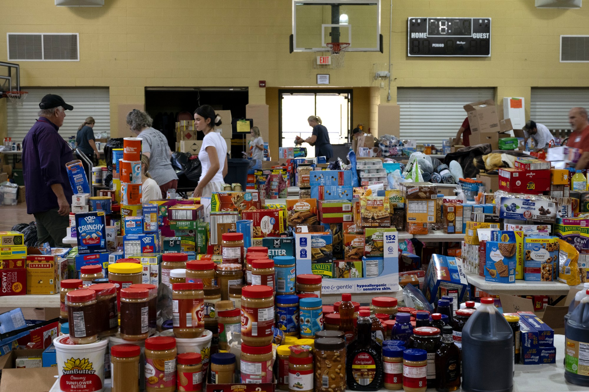 Jars of peanut butter, boxes of granola bars, and other food, are stacked in a messy pile in a gymnasium