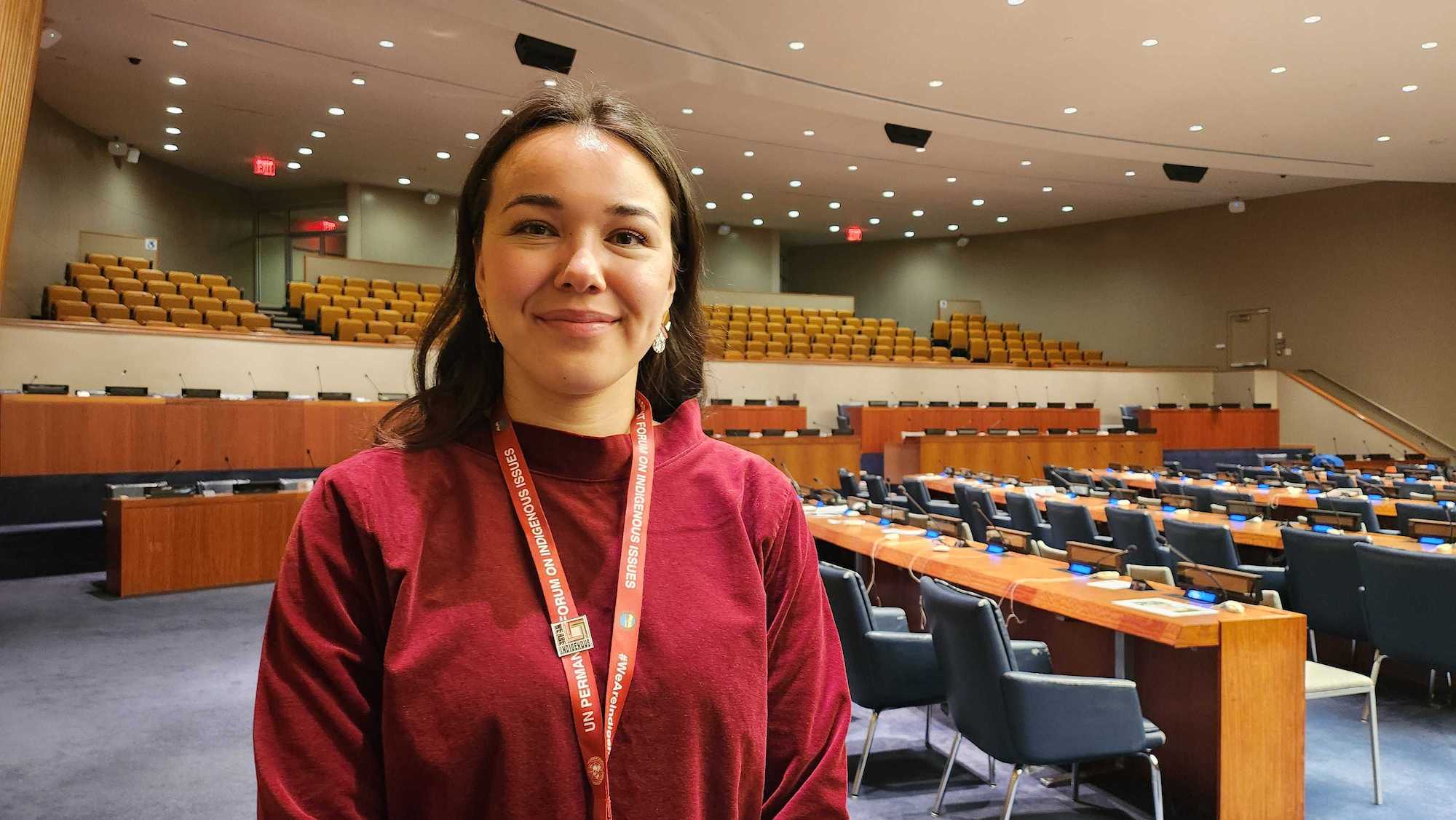 a woman wears a UN badge in a room with lots of chairs and tables