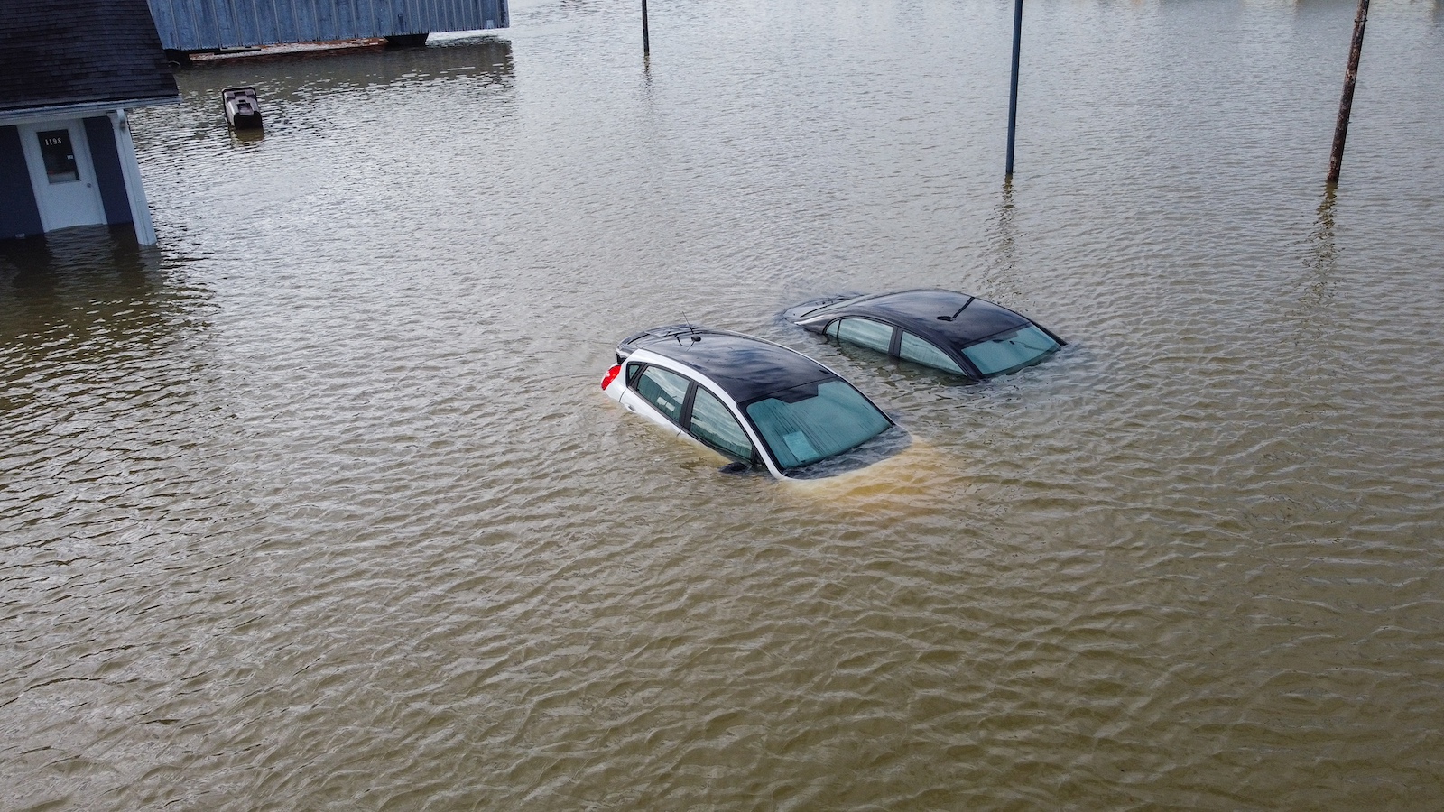 Aerial view of two cars half-submerged in brownish, murky floodwater