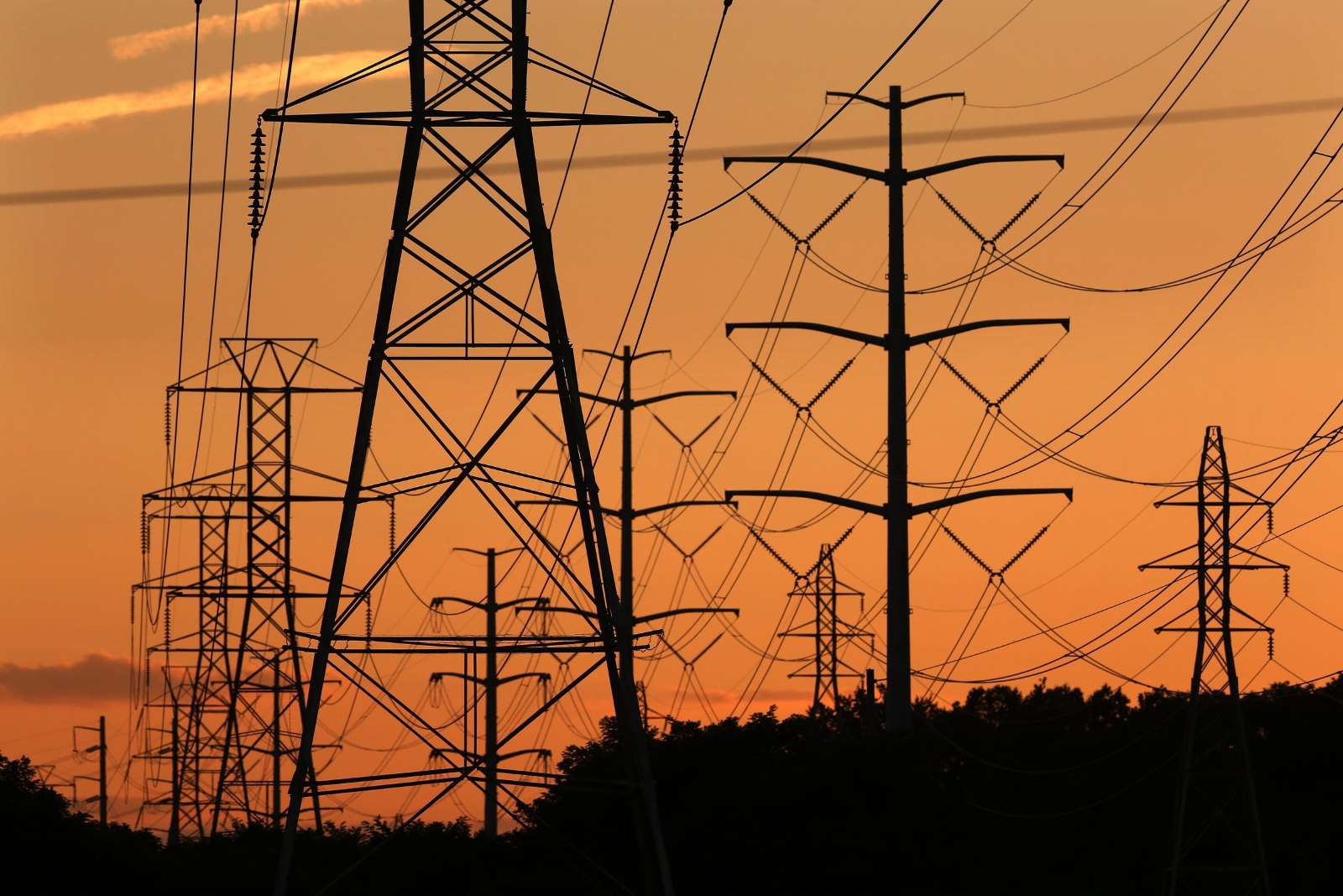 Silhouettes of power transmission lines are seen illuminated against a sunset