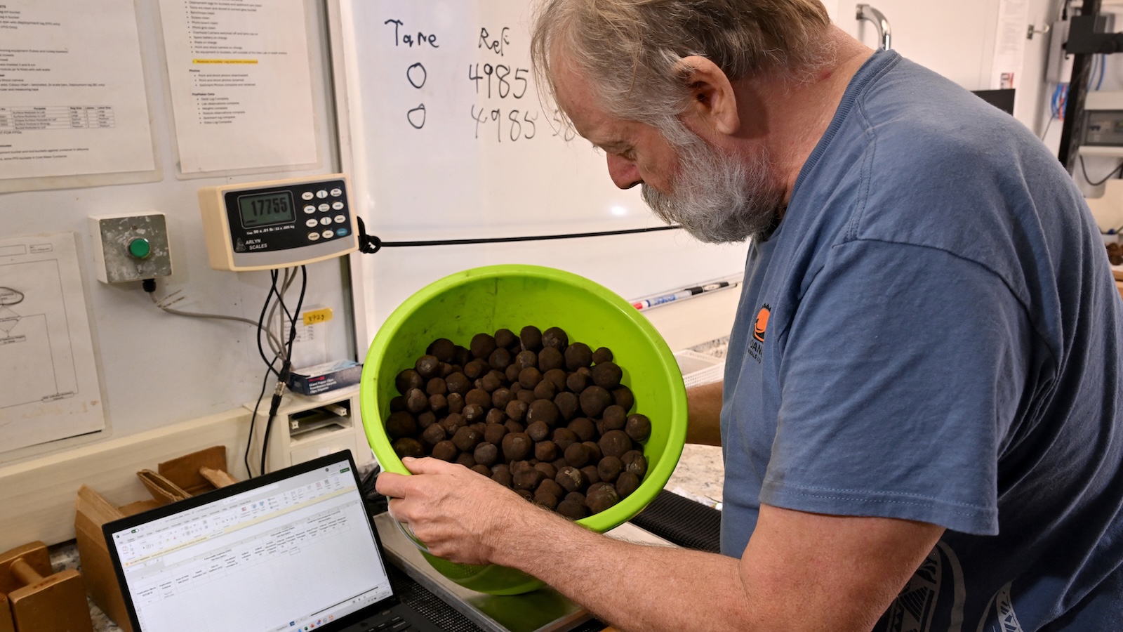 A geologist inspects a bucket of polymetallic nodules, misshapen black globes encrusted with metals like <span class='tooltipsall tooltipsincontent classtoolTips10'/>cobalt, <span class='tooltipsall tooltipsincontent classtoolTips9'>nickel</span> and manganese.” data-caption=”A geologist inspects a bucket of polymetallic nodules, misshapen black globes encrusted with metals like cobalt, nickel, and manganese, collected by the research vessel MV Anuanua Moana from near the Cook Islands.<br>