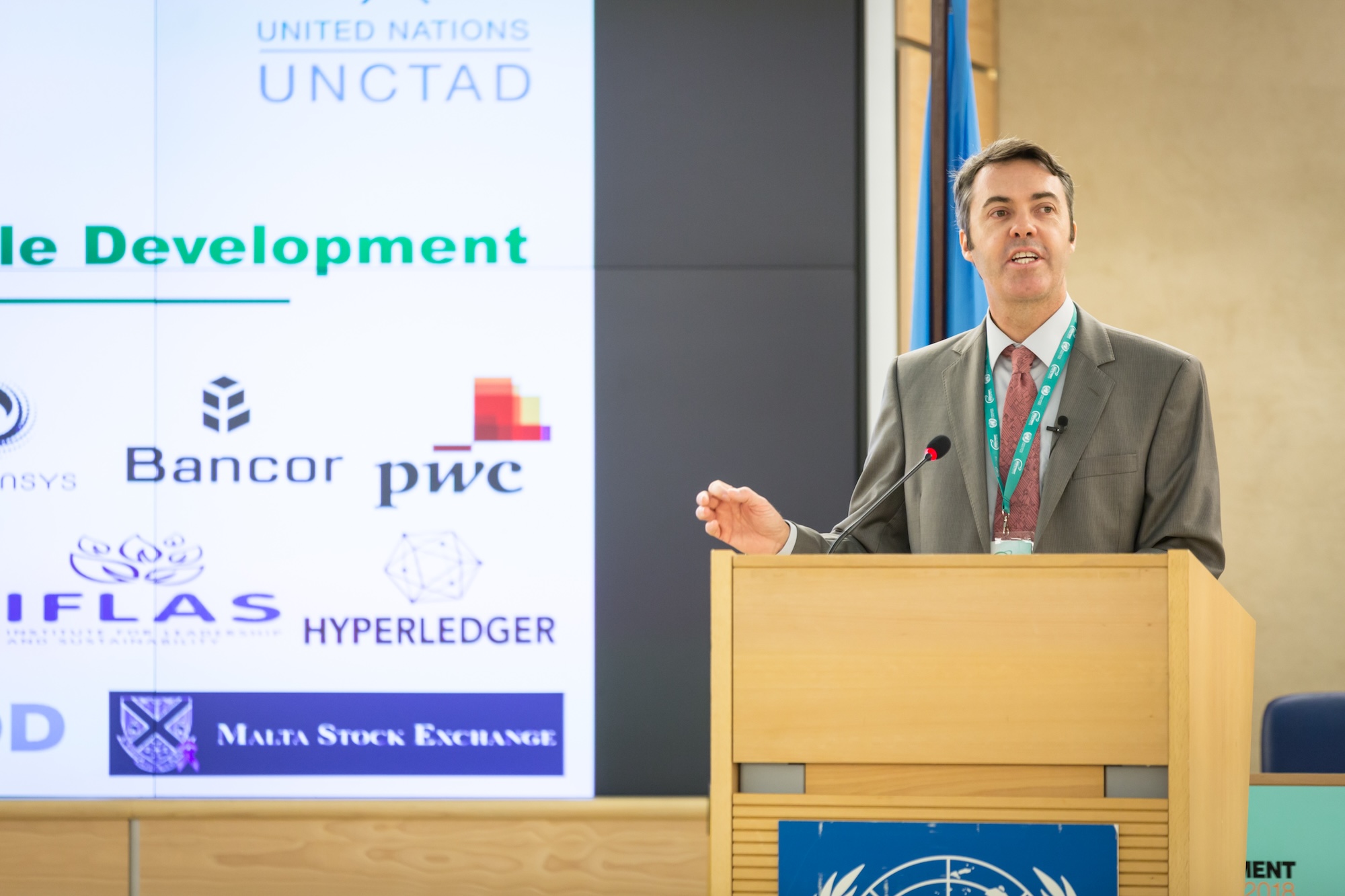 A man in a suit presents at a podium by a power point presentation screen