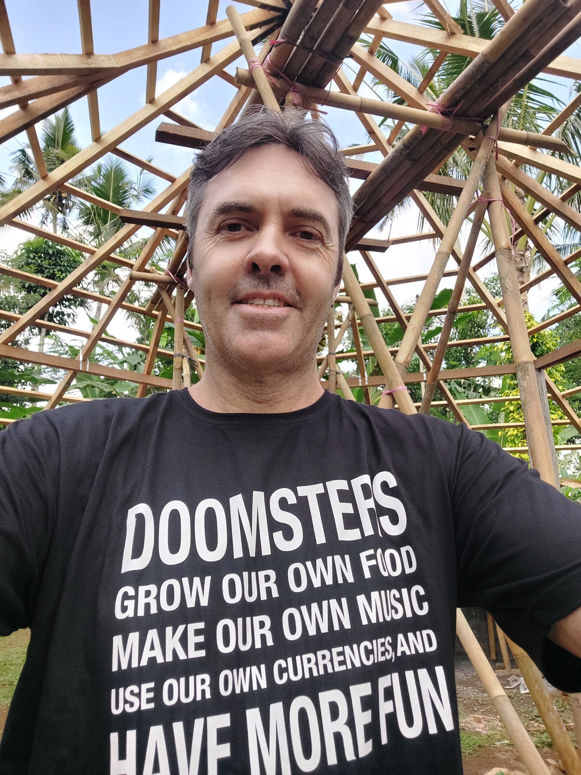 a man in a shirt that says doomsters grow our own food make our own music use our own currencies and have more fun